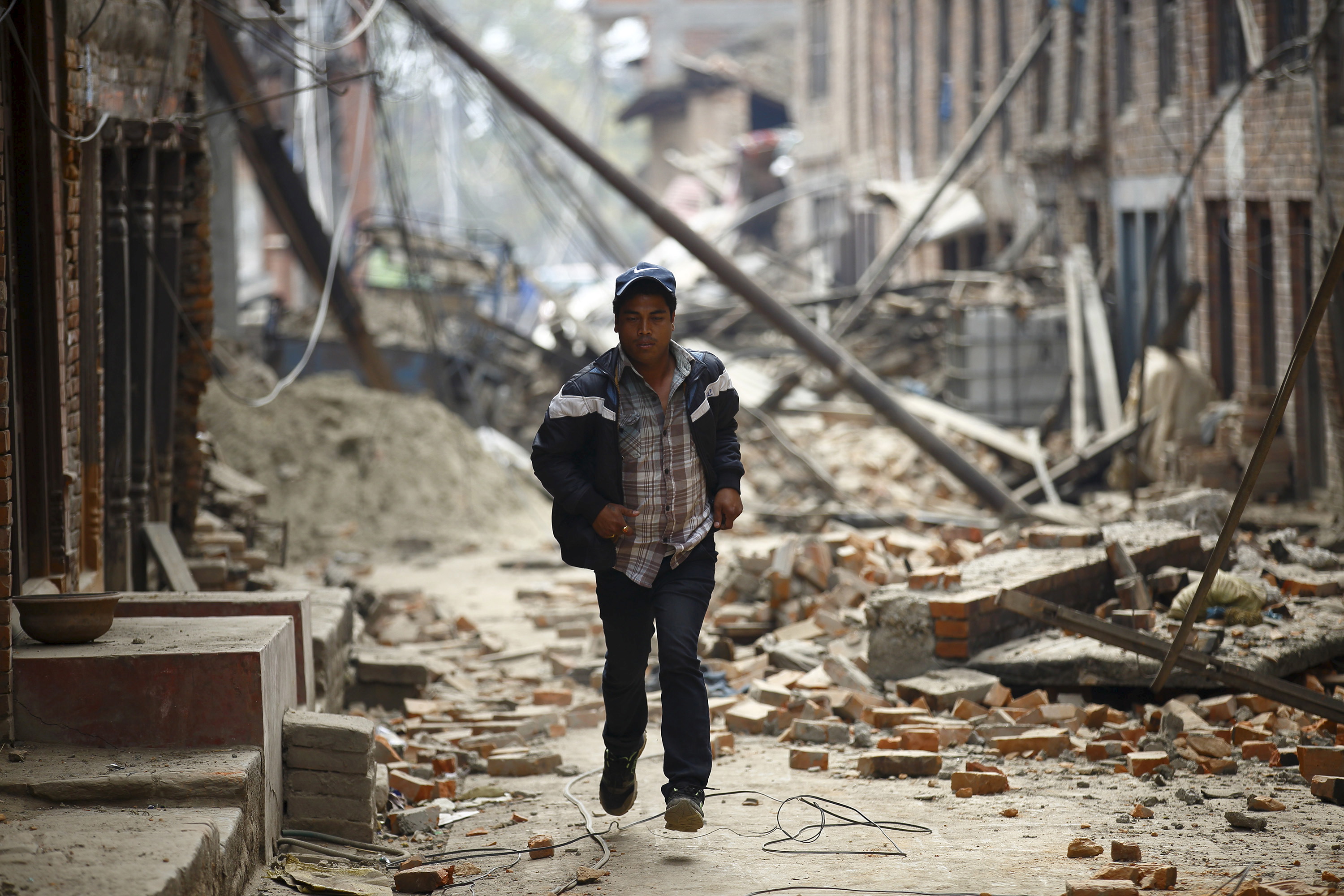 Man runs past damaged houses as aftershocks of an earthquake are felt a day after the earthquake in Bhaktapur